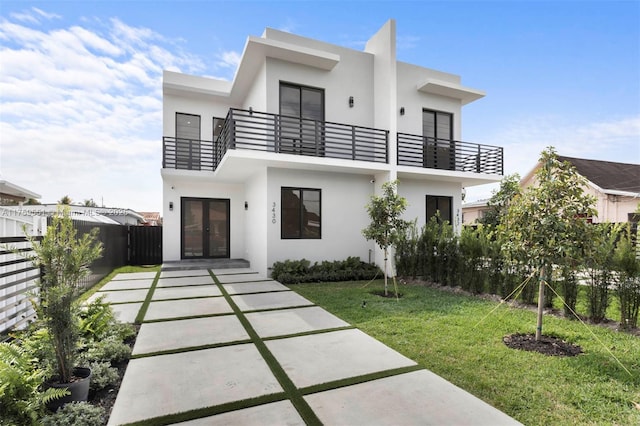 view of front of house with a balcony, fence, french doors, stucco siding, and a front yard