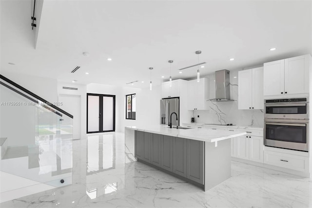 kitchen with white cabinets, marble finish floor, stainless steel appliances, light countertops, and wall chimney range hood