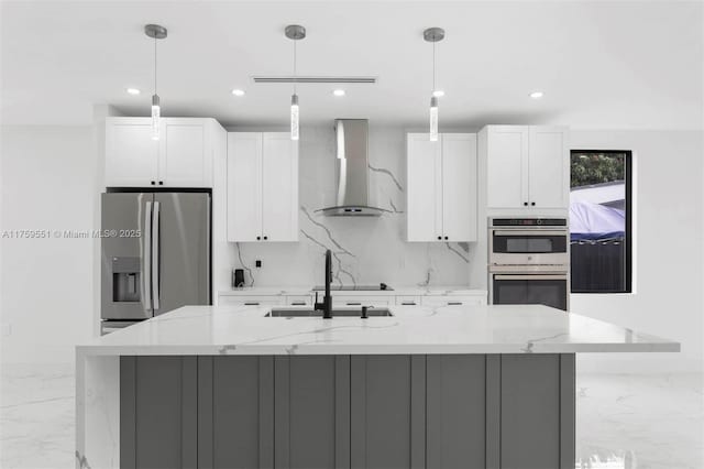 kitchen featuring marble finish floor, appliances with stainless steel finishes, a kitchen island with sink, white cabinetry, and wall chimney range hood