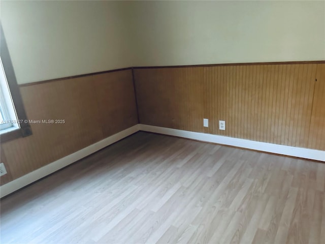 unfurnished room featuring baseboards, wood finished floors, and wainscoting