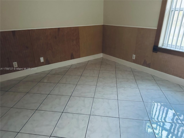 empty room featuring wood walls, light tile patterned flooring, and wainscoting