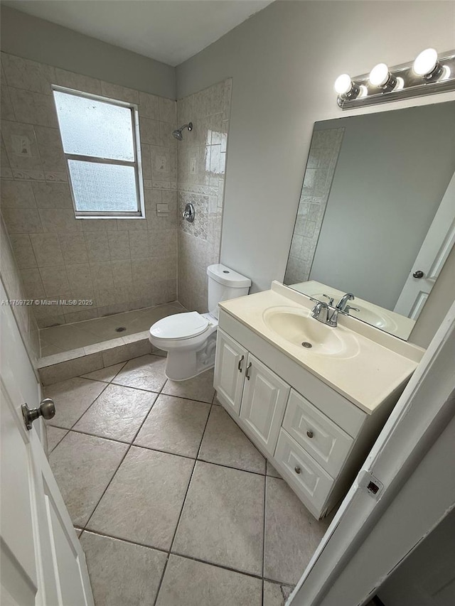 bathroom with a tile shower, toilet, tile patterned floors, and vanity