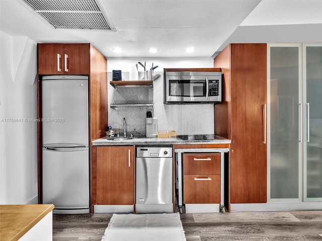 kitchen featuring stainless steel appliances, wood finished floors, a sink, visible vents, and brown cabinetry