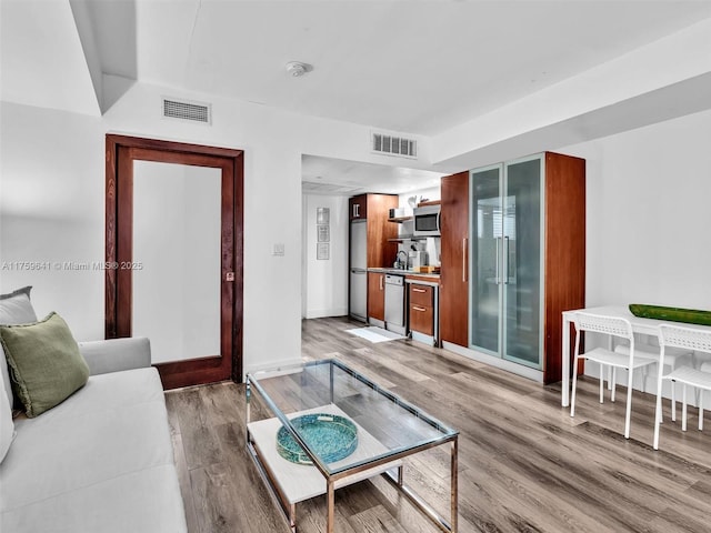 living room with light wood-type flooring, visible vents, and baseboards