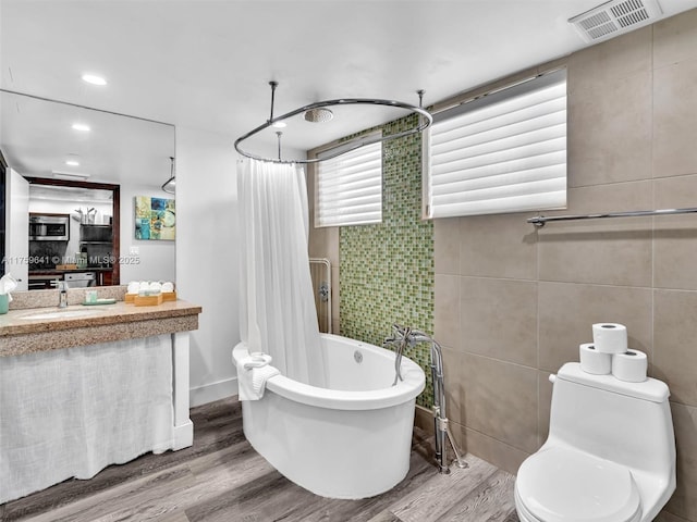 full bathroom with tile walls, visible vents, a freestanding bath, toilet, and wood finished floors