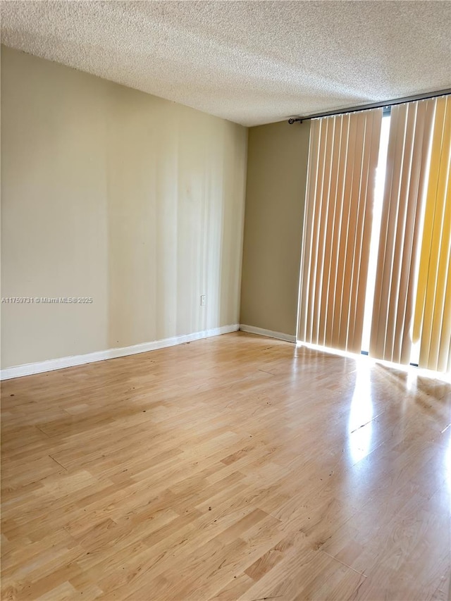 empty room featuring a textured ceiling, baseboards, and light wood-type flooring