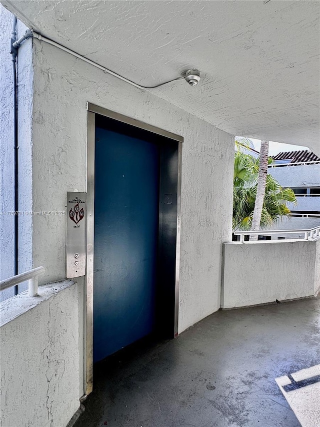 property entrance with elevator, a balcony, and stucco siding