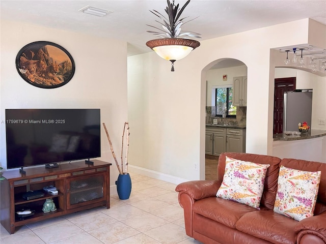 living area featuring arched walkways, visible vents, baseboards, and light tile patterned floors