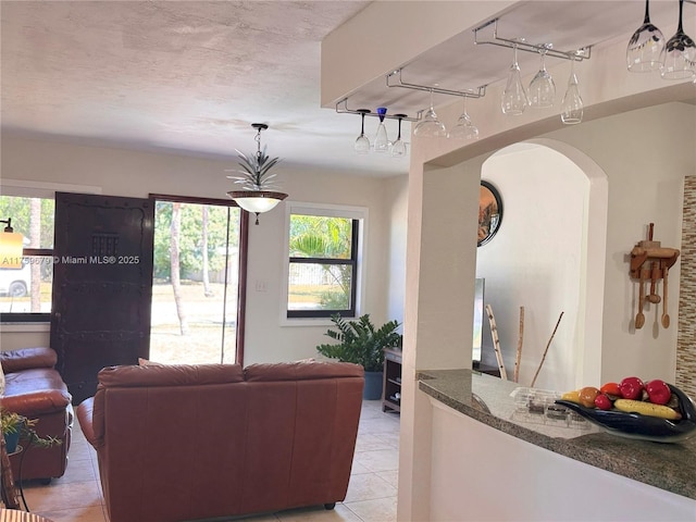 living area with arched walkways, a textured ceiling, and light tile patterned flooring