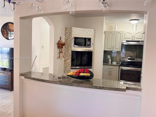 kitchen with light tile patterned flooring, under cabinet range hood, stainless steel appliances, visible vents, and tasteful backsplash