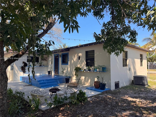 view of front of house featuring central AC unit, a fire pit, a patio, fence, and stucco siding