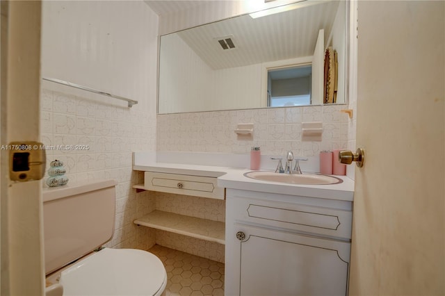 bathroom with toilet, visible vents, tile walls, and vanity