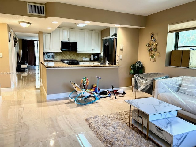 kitchen with a peninsula, black fridge with ice dispenser, visible vents, baseboards, and decorative backsplash