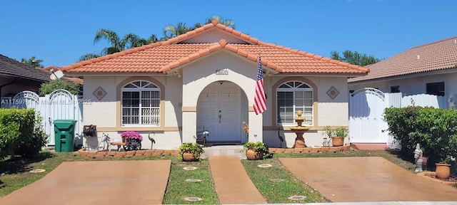 mediterranean / spanish house with a tiled roof, a gate, fence, and stucco siding