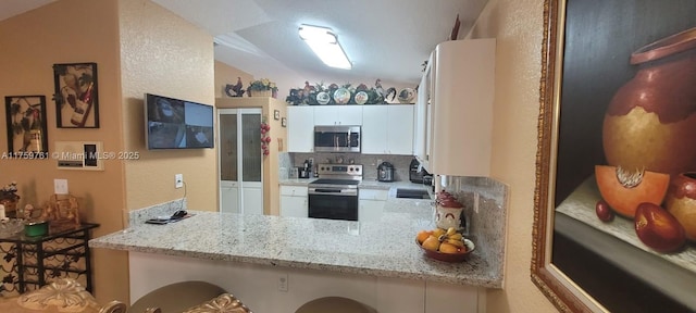 kitchen with tasteful backsplash, appliances with stainless steel finishes, a peninsula, light stone countertops, and white cabinetry