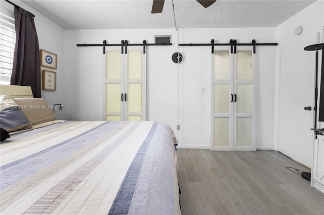 unfurnished bedroom featuring a barn door, visible vents, a ceiling fan, wood finished floors, and a textured ceiling