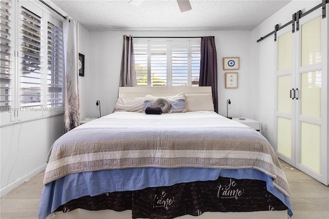 bedroom featuring a barn door, a textured ceiling, a ceiling fan, and wood finished floors