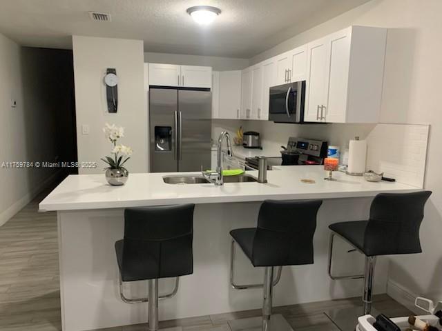 kitchen with a peninsula, a sink, stainless steel appliances, light countertops, and a kitchen bar