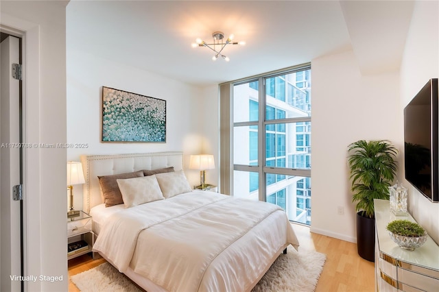 bedroom with light wood-style floors, baseboards, and a wall of windows