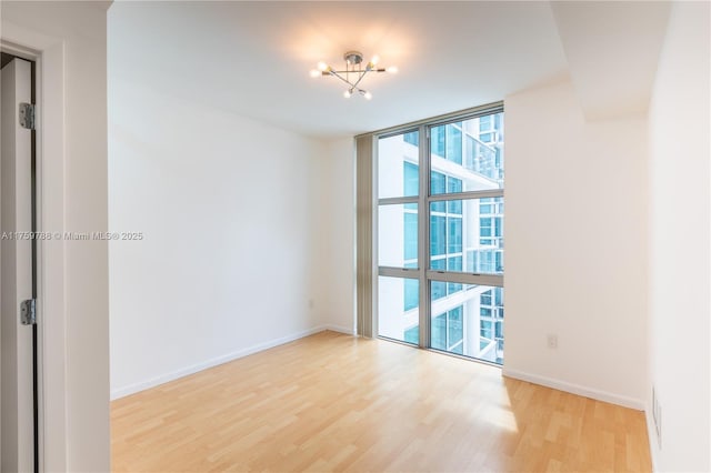 unfurnished room featuring a wall of windows, light wood-type flooring, and baseboards