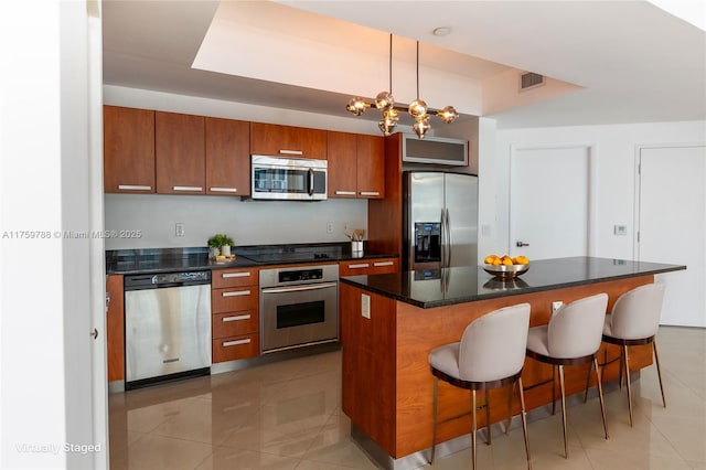 kitchen featuring stainless steel appliances, brown cabinets, visible vents, and a kitchen bar