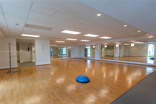 workout area featuring a paneled ceiling, baseboards, and wood finished floors