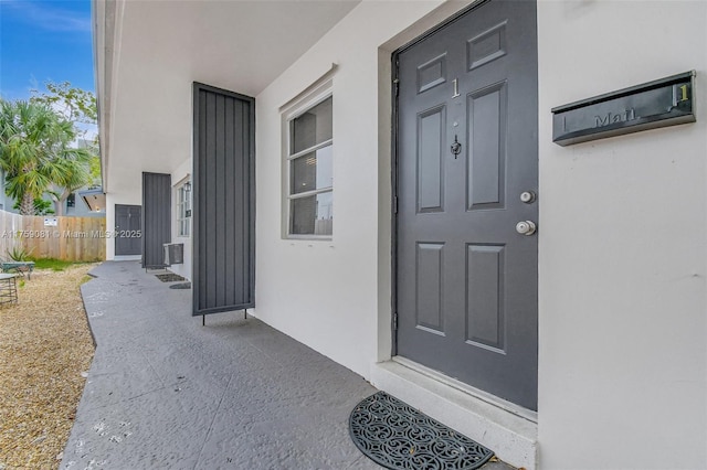 entrance to property with fence, central AC, and stucco siding