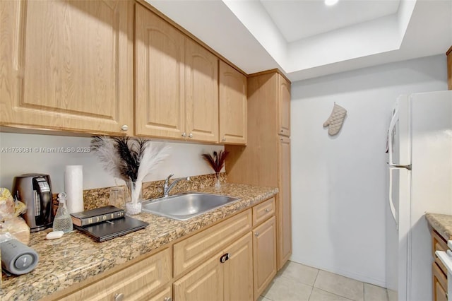 kitchen with freestanding refrigerator, light tile patterned floors, a sink, and light brown cabinetry