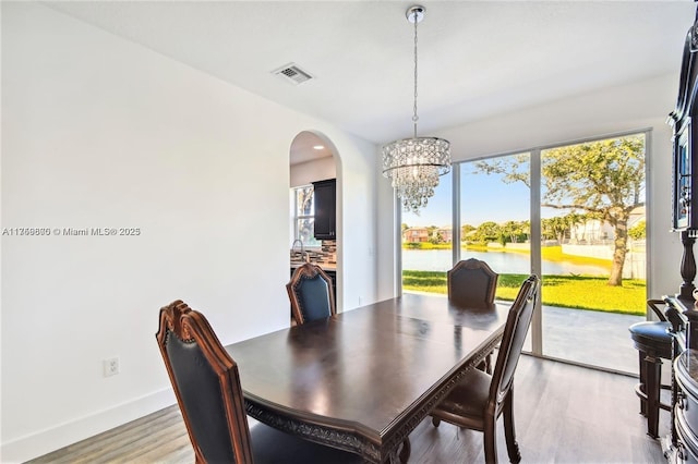 dining room with baseboards, arched walkways, light wood-style flooring, a water view, and an inviting chandelier