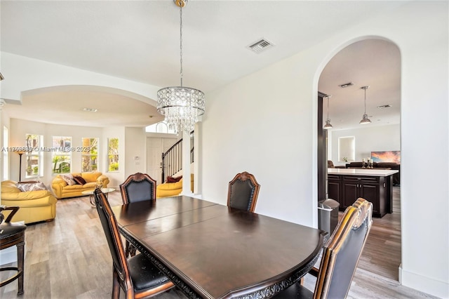 dining space with arched walkways, a notable chandelier, visible vents, light wood-style flooring, and stairs