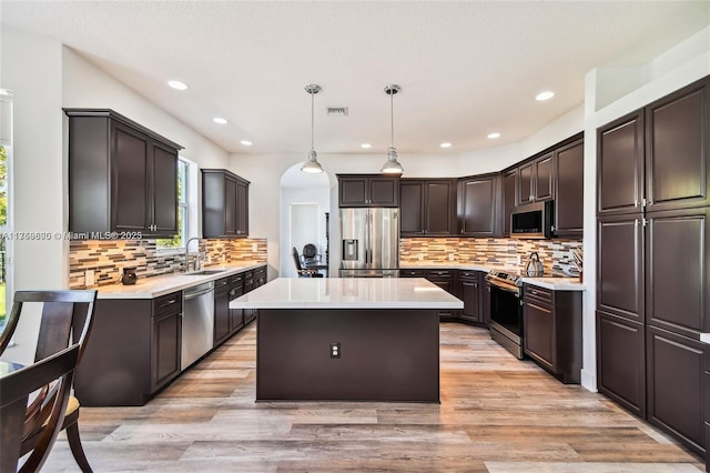 kitchen with light countertops, appliances with stainless steel finishes, a kitchen island, a sink, and light wood-type flooring