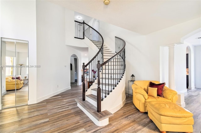 staircase featuring arched walkways, a high ceiling, baseboards, and wood finished floors