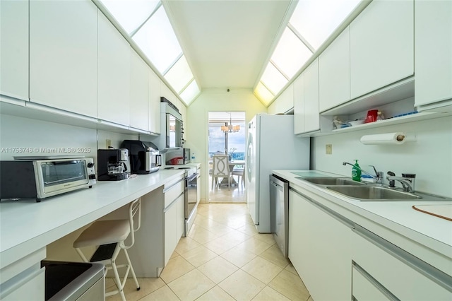 kitchen with stainless steel appliances, vaulted ceiling, white cabinetry, and a sink