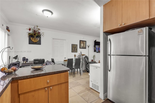 kitchen featuring light tile patterned floors, dark stone counters, crown molding, and freestanding refrigerator