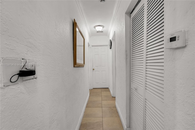 corridor with baseboards, light tile patterned flooring, and a textured wall