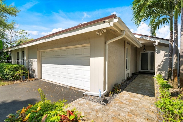 view of side of property with aphalt driveway, stucco siding, and a garage