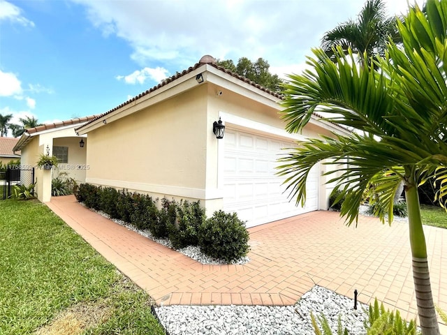 view of side of home with a garage, a tiled roof, fence, and stucco siding