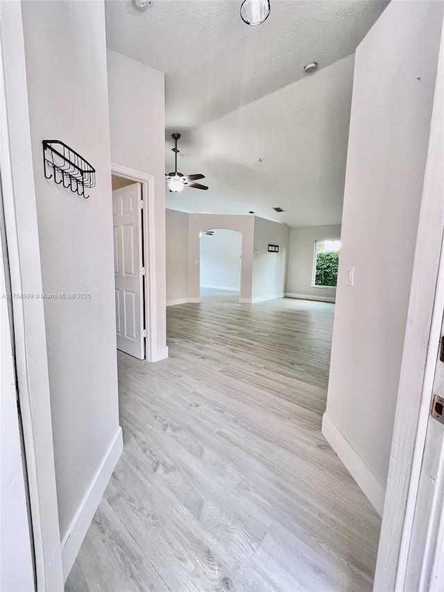 spare room featuring light wood finished floors, baseboards, arched walkways, ceiling fan, and a textured ceiling