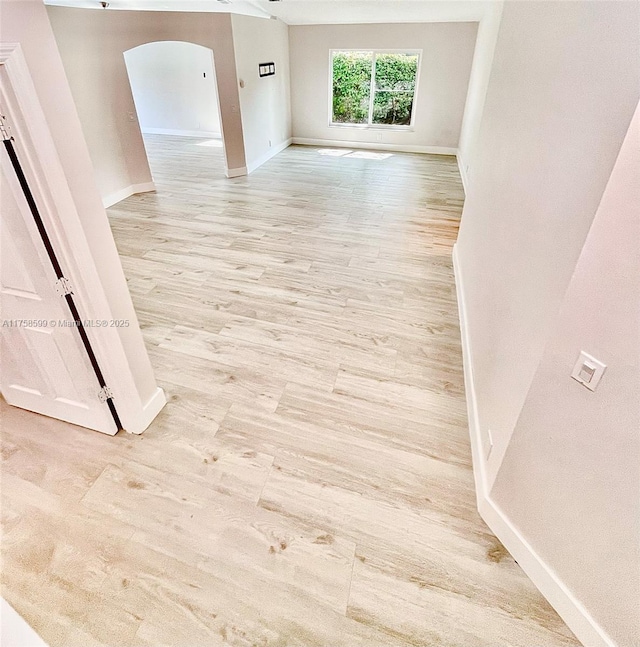 empty room with light wood-style flooring, arched walkways, and baseboards