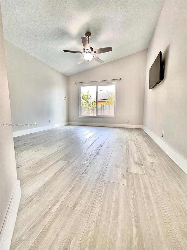 empty room with light wood-type flooring, ceiling fan, lofted ceiling, and baseboards