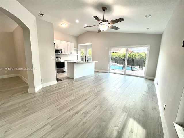 unfurnished living room with arched walkways, lofted ceiling, a ceiling fan, a sink, and light wood-type flooring