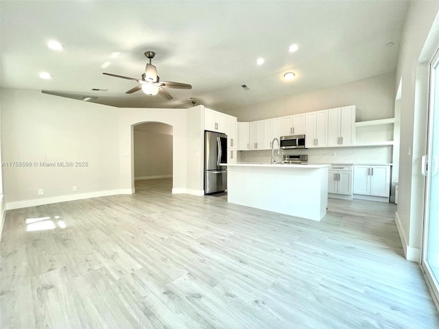 kitchen featuring arched walkways, appliances with stainless steel finishes, open floor plan, light wood-style floors, and open shelves