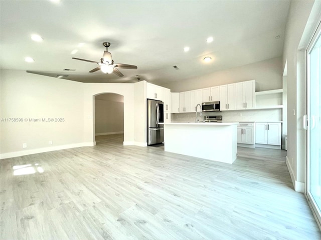 kitchen featuring light wood finished floors, arched walkways, open floor plan, stainless steel appliances, and open shelves