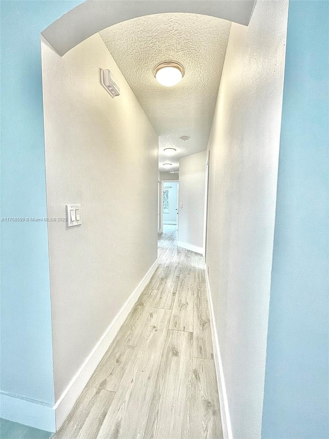 hallway with a textured ceiling, baseboards, arched walkways, and light wood-style floors