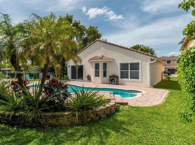 back of property featuring a patio, a yard, a tiled roof, an outdoor pool, and stucco siding