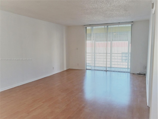 empty room featuring floor to ceiling windows, a textured ceiling, baseboards, and wood finished floors