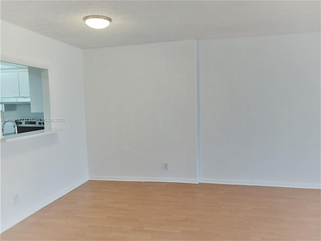 unfurnished room featuring light wood-type flooring, a textured ceiling, and baseboards