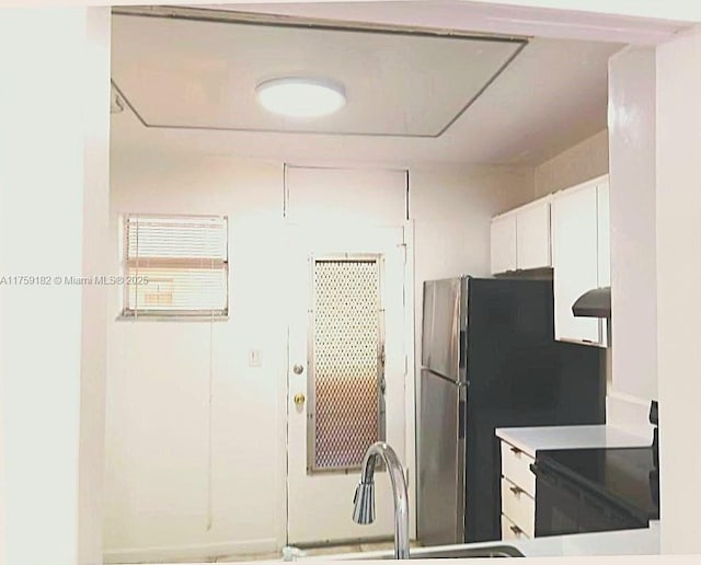 kitchen featuring stove, a sink, white cabinets, light countertops, and freestanding refrigerator