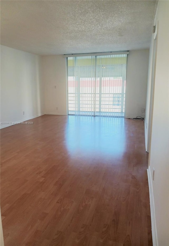 empty room featuring a wall of windows, a textured ceiling, baseboards, and wood finished floors