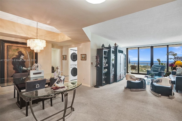 carpeted living area with stacked washer and clothes dryer, a textured ceiling, floor to ceiling windows, baseboards, and a chandelier